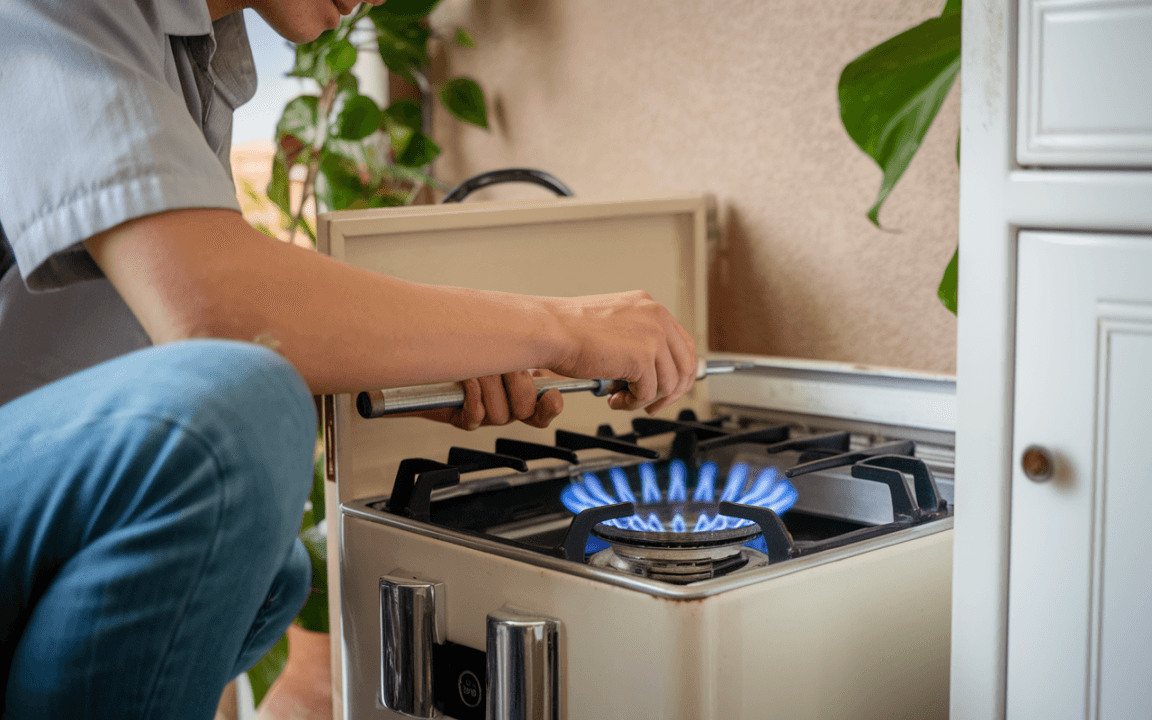 Personne ajustant un brûleur de gaz avec une clé, flamme bleue visible, dans une cuisine lumineuse et végétalisée.