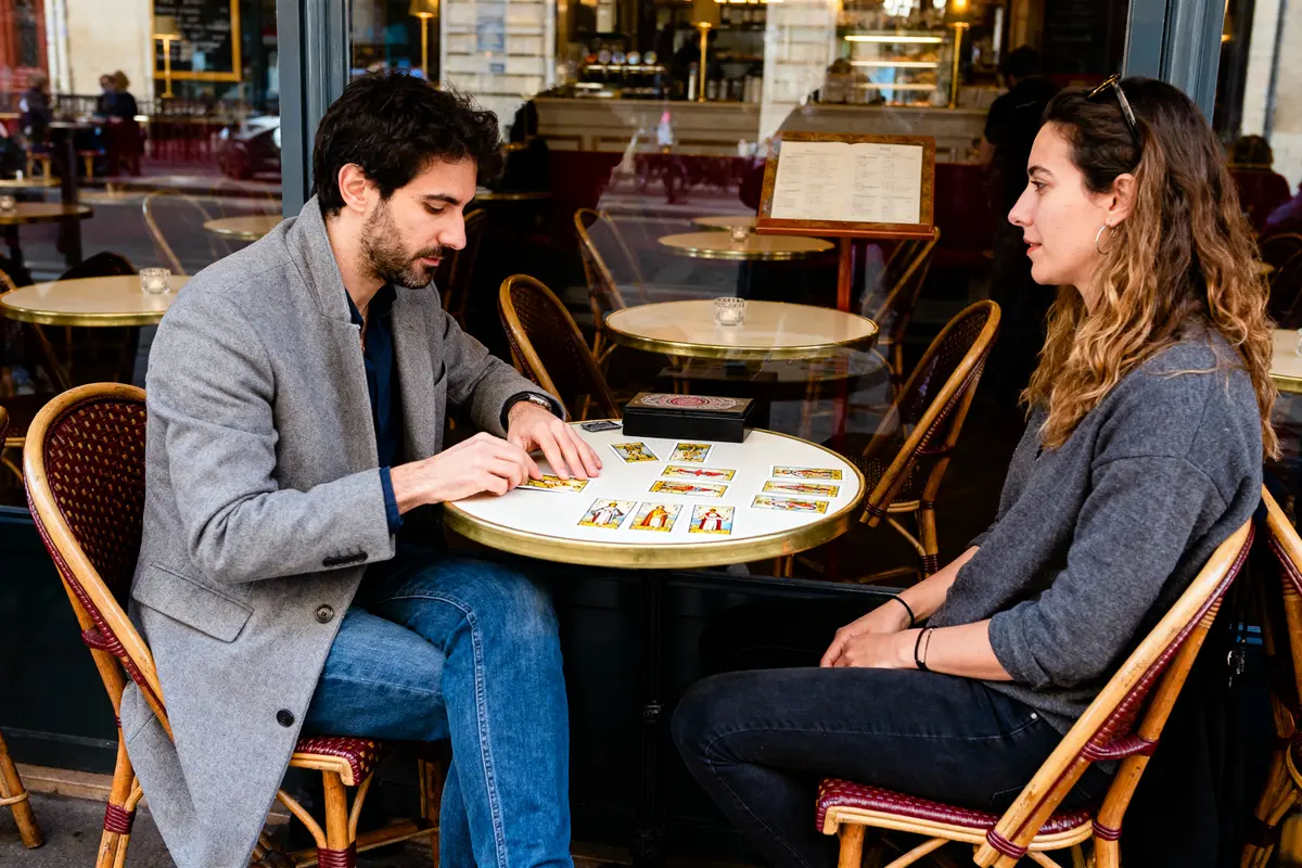 Deux personnes lisant des cartes de tarot à une table de café extérieur, conversation calme et concentrée.