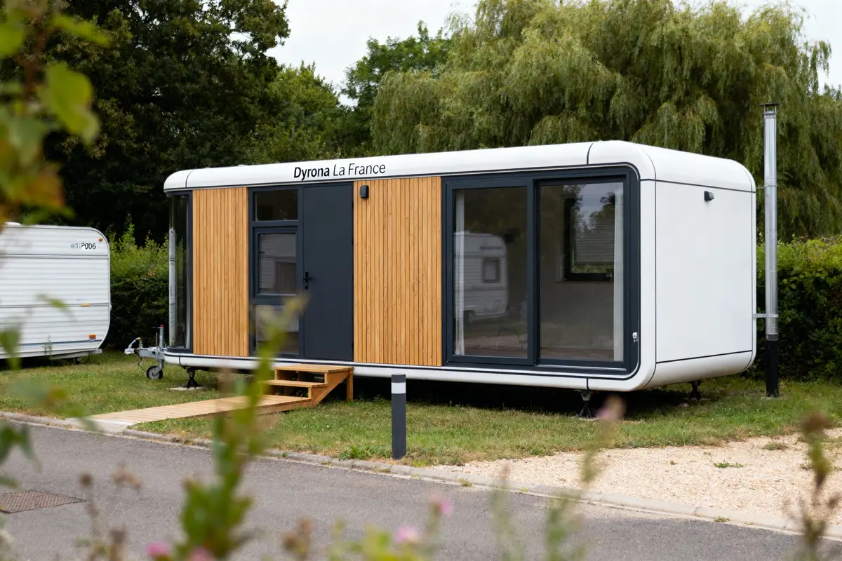 Tiny house moderne avec bardage bois, grandes fenêtres et terrasse, entourée de verdure et d'un autre mobil-home.