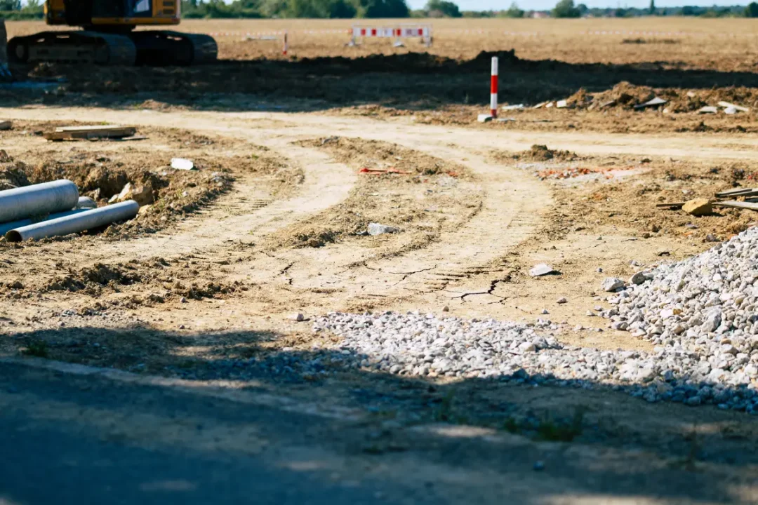 Chantier de construction avec engin, tuyaux métalliques, terre remuée et gravats, sous un ciel dégagé.