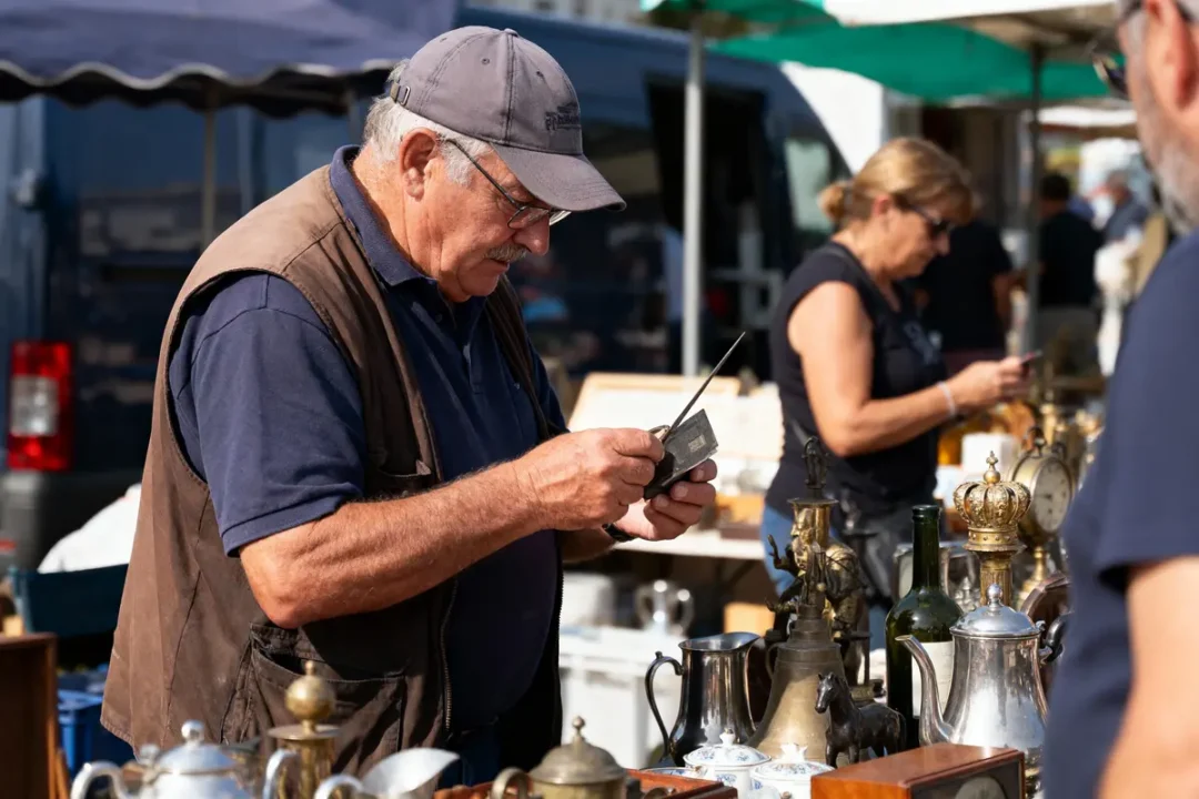 Homme examinant un objet ancien dans un marché aux puces, avec divers objets exposés sur la table.