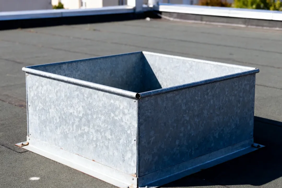 Boîte métallique carrée sur un toit plat ensoleillé avec parapet en arrière-plan.