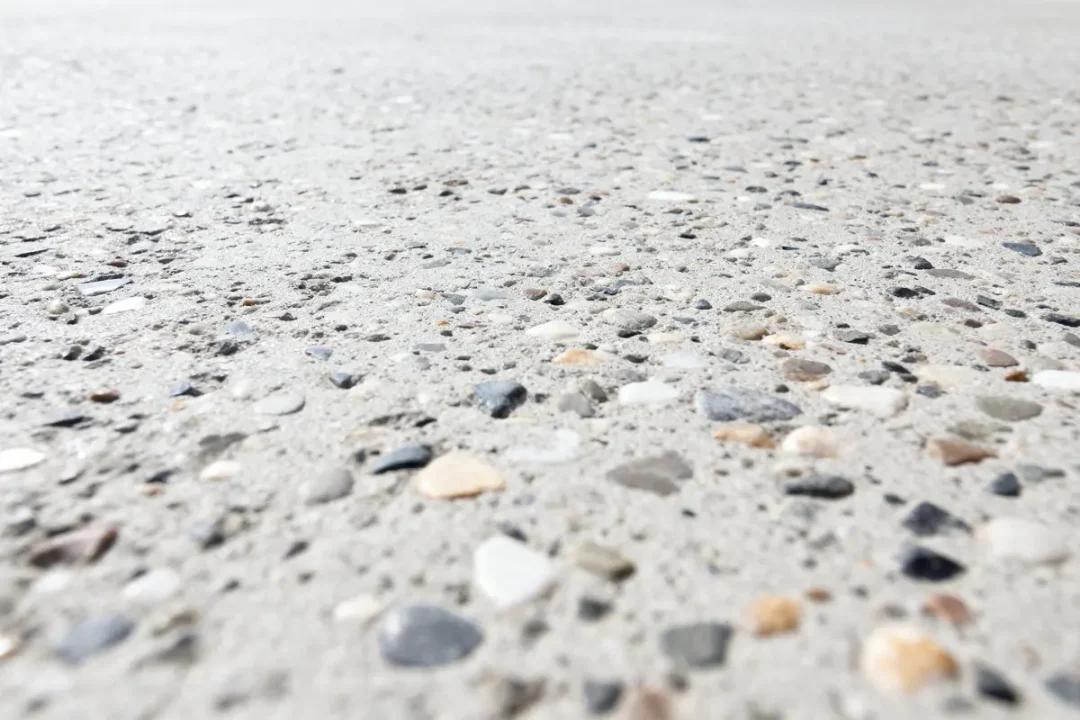 Gros plan d'une surface en béton granuleuse avec des cailloux de différentes couleurs incrustés.