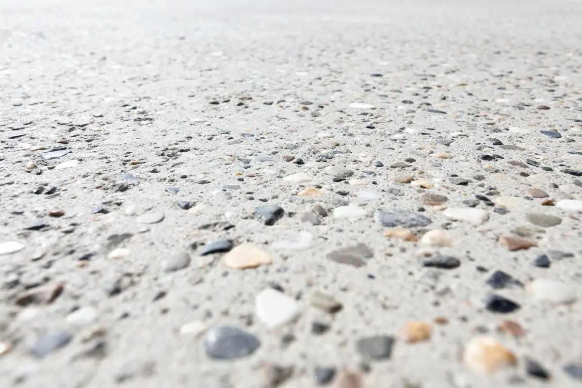 Gros plan d'une surface en béton granuleuse avec des cailloux de différentes couleurs incrustés.
