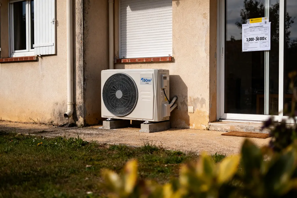 Climatiseur extérieur installé sur socle béton, proche fenêtre maison avec volet roulant fermé.