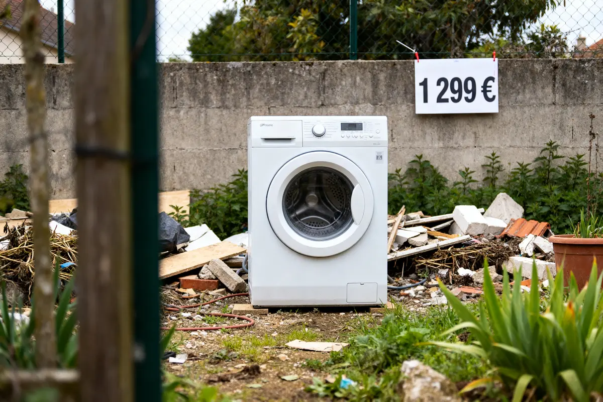Sèche-linge pompe à chaleur inconvénient, abandonné dans un jardin avec débris et prix affiché.