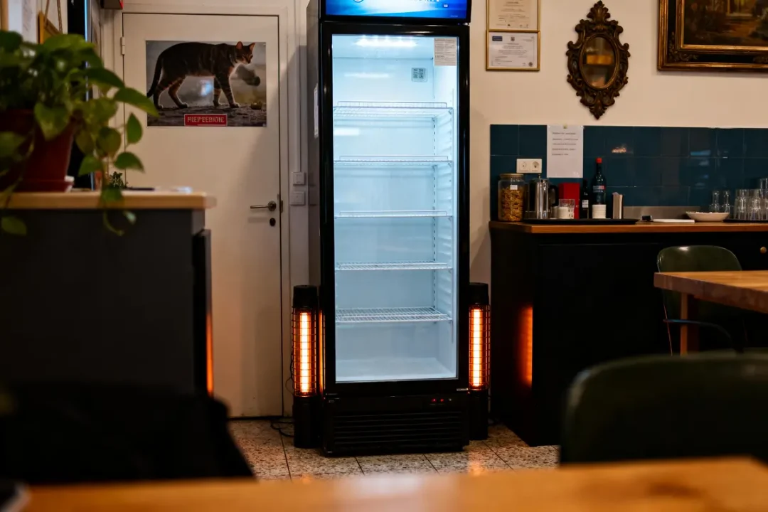 Frigo vide entouré de chauffages dans une pièce avec décoration de style classique et poster de chat.